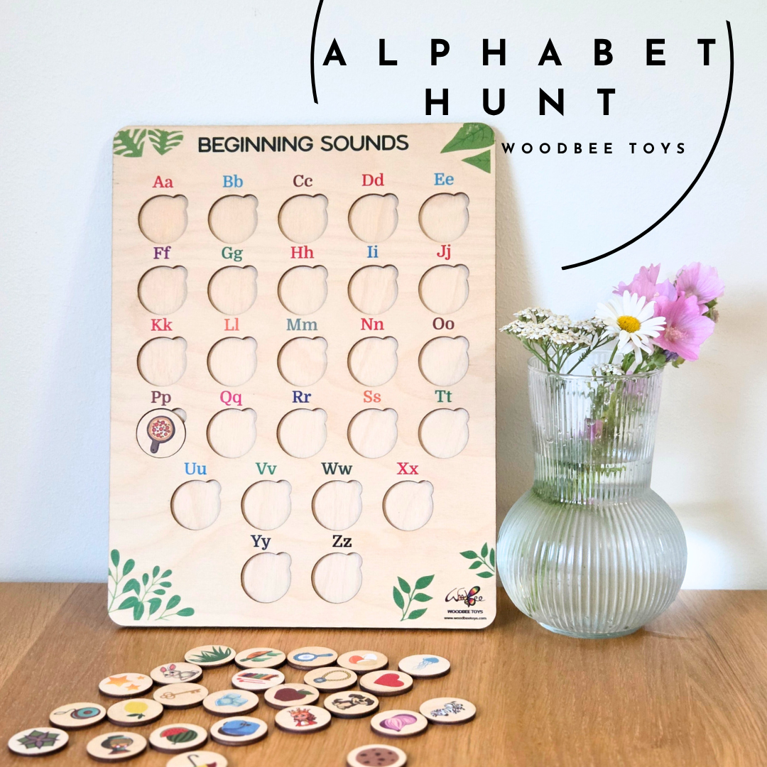 Wooden alphabet board game with letters and beginning sounds, next to a vase with flowers on a wooden surface.