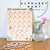 Wooden alphabet board game with letters and beginning sounds, next to a vase with flowers on a wooden surface.