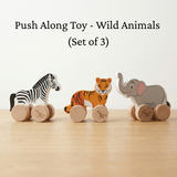 Set of three wooden push along toys shaped like a zebra, tiger, and elephant on a light wood surface.