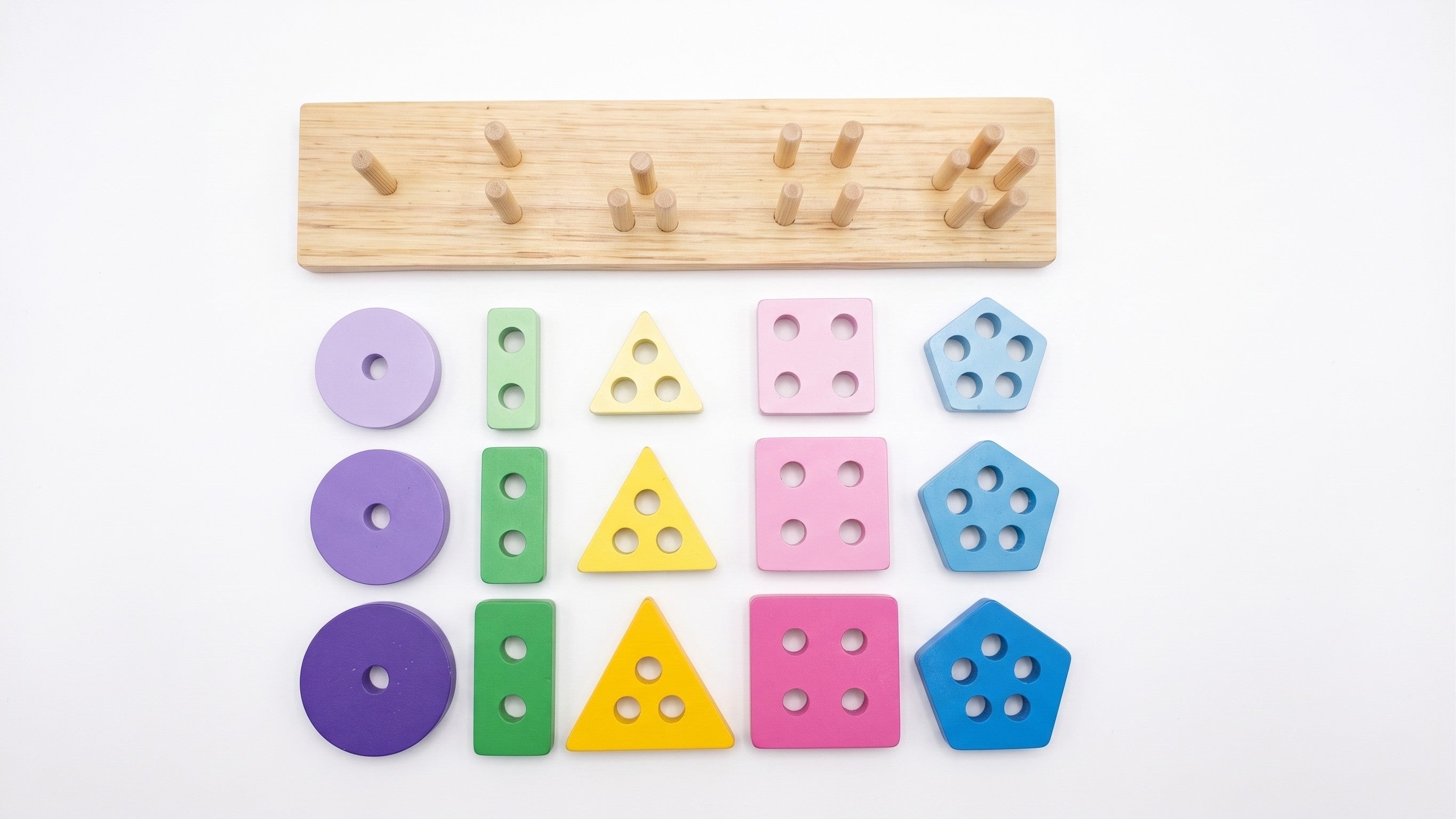 All 15 pieces of the wooden geometric shape stacker laid out by shape and colour beside the pegged wooden base board